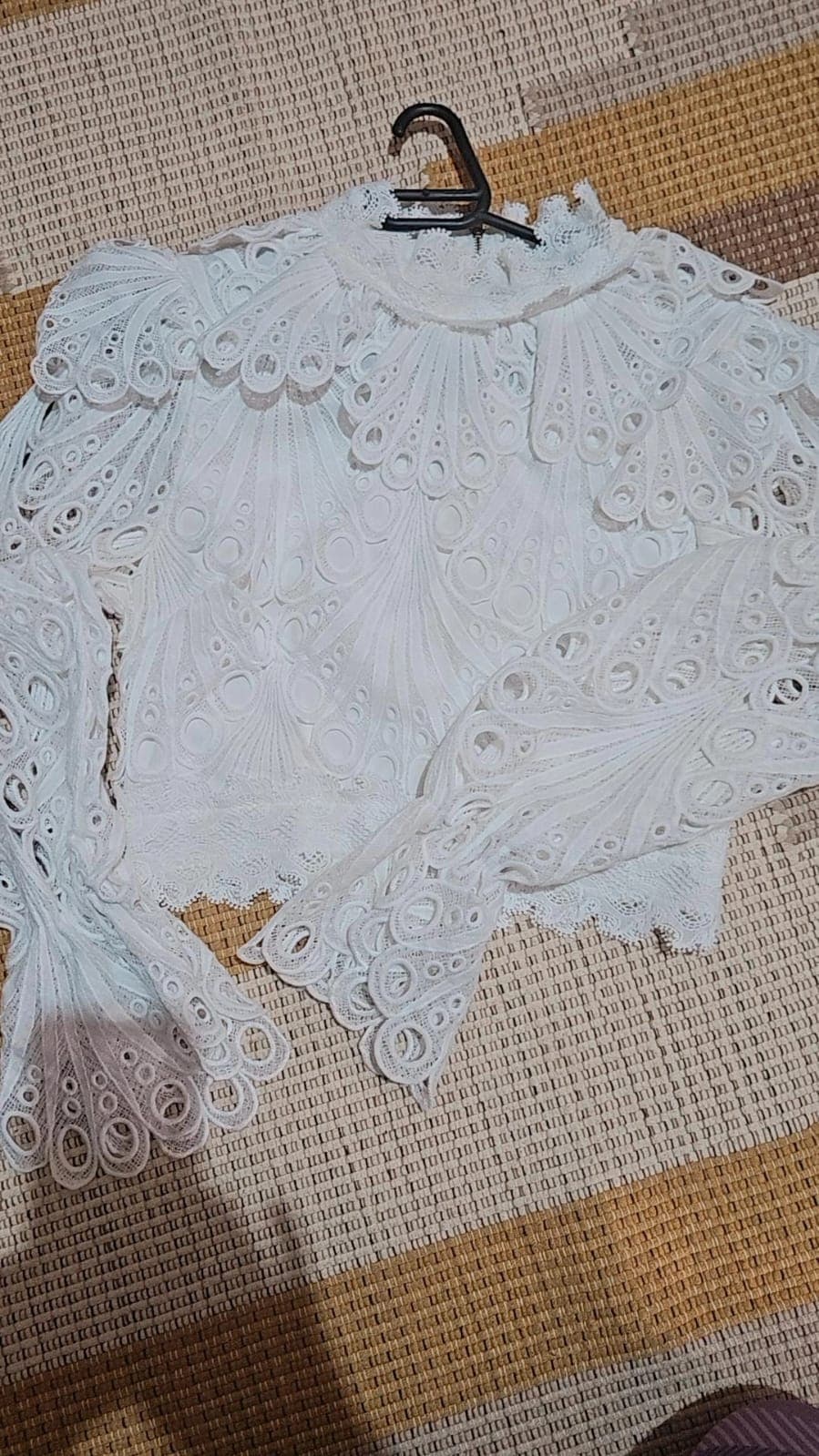 Bata branca de renda vazada com gola alta franzida, mangas sino longas e barra recortada em ondas