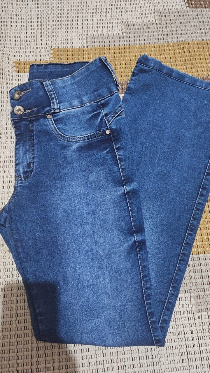 Calça jeans azul dobrada, mostrando o cós de dois botões e a boca flare