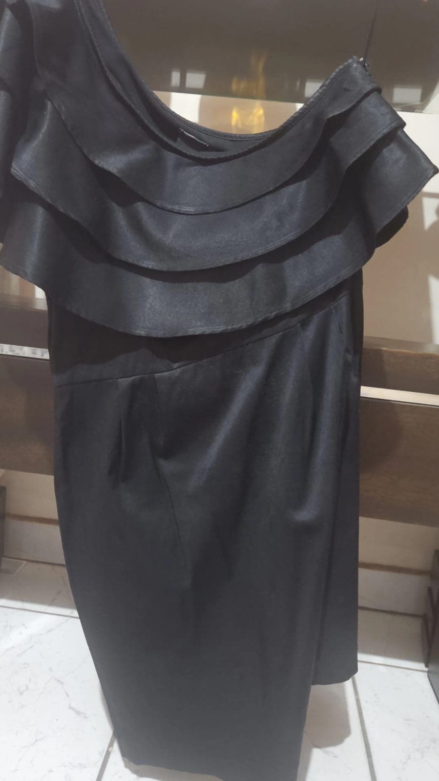Vestido tubinho preto acetinado em um ombro só, com três babados em camadas atravessando o busto