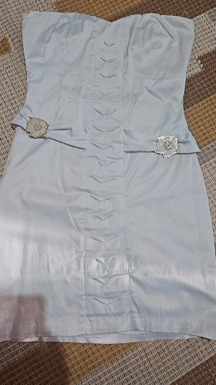 Vestido tomara que caia em azul muito claro, com pregas verticais no centro da frente e duas flores de strass marcando a cintura