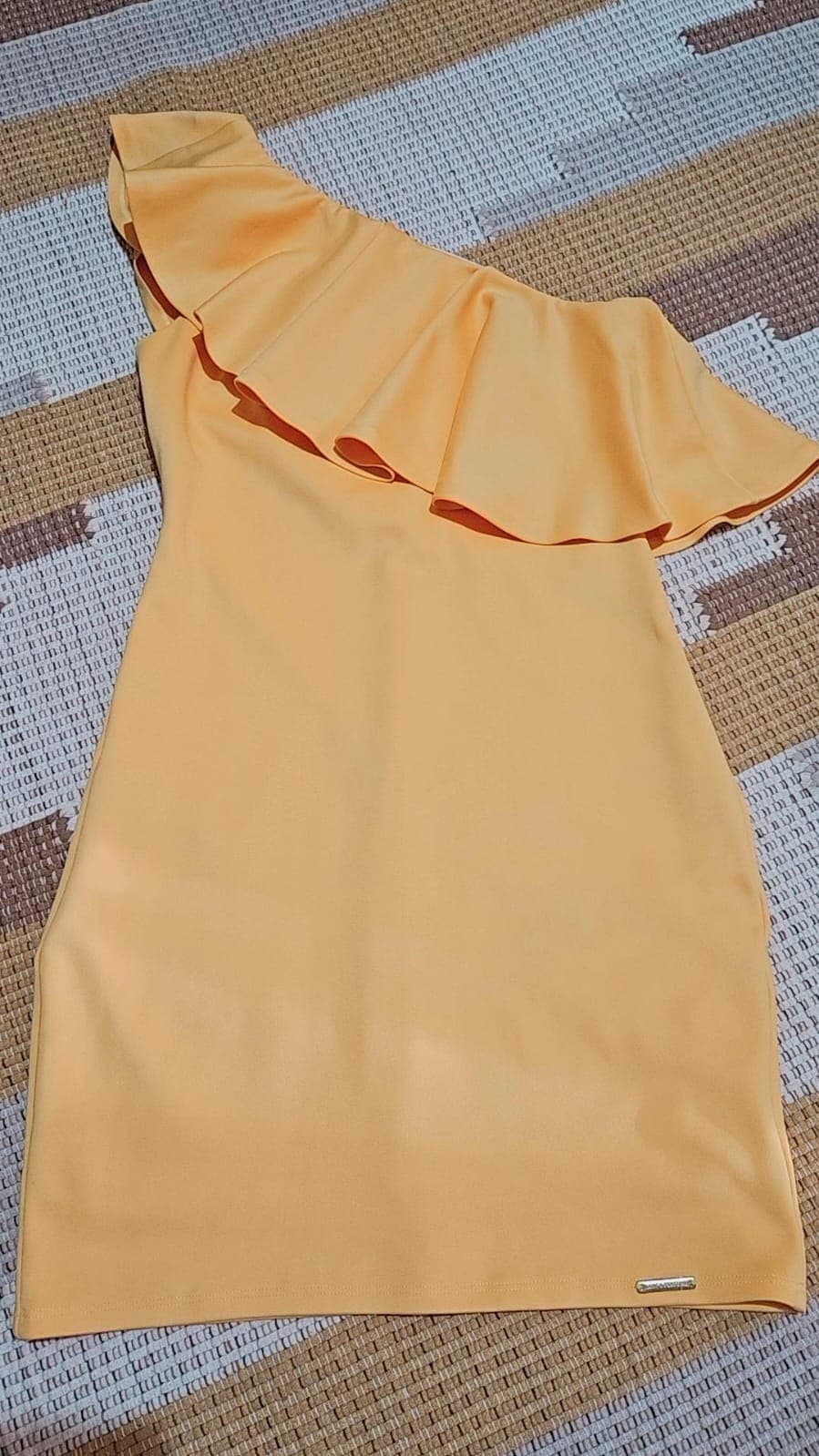 Vestido curto em tom amarelo-âmbar, ombro único com babado largo atravessando o busto, tecido de crepe liso